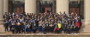 Over 100 middle school students in matching green shirts and adults in matching blue shirts stand on stone steps in front of building with large columns