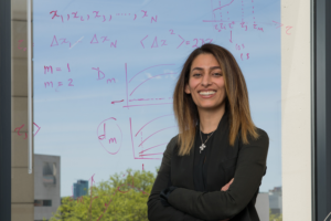 woman with dark shoulder lenght hair in front of a window covered in mathematics