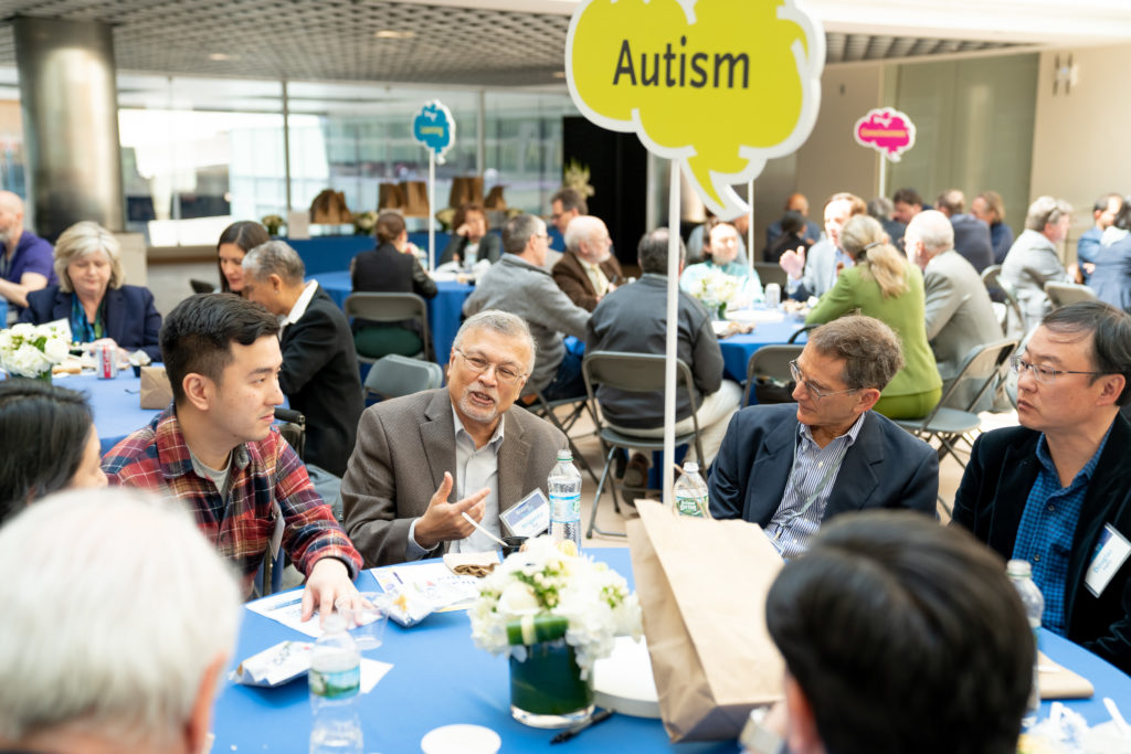 several people chat at a table with an "Autistm" sign