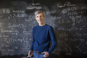 man in front of a chalkboard covered in equations