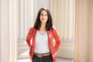 Photo of Juncal Arbelaiz wearing an orange cardigan in front of large white pillars at MIT