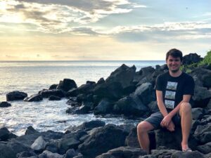 Timur Cinay sitting on a cluster of rocks in front of the ocean