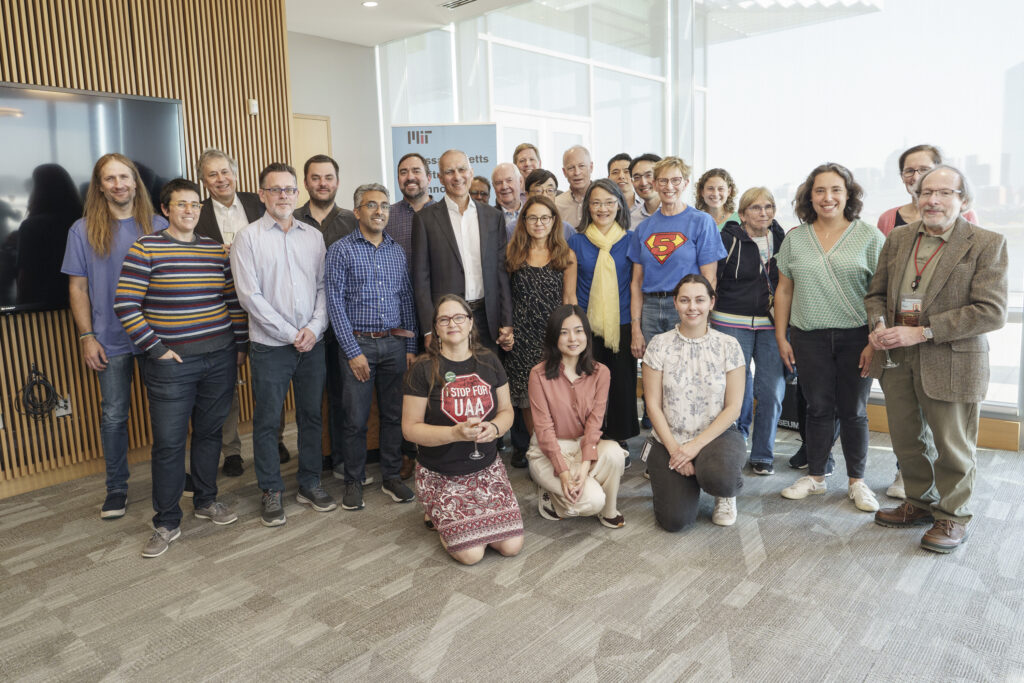 Professor Moungi Bawendi stands smiling with his wife, surrounded by two dozen colleagues