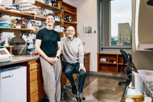 Amy Keating stands smiling beside Jay A. Stein, who is seated in a biology laboratory.